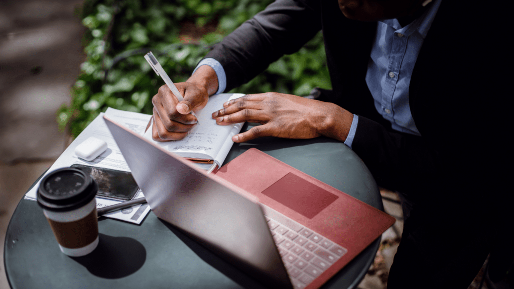 man writing article on his desk and laptop